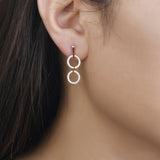 unique jewelry, unique earrings, fashion jewelry, fashion earrings, diamond earrings in rose gold, dangling earrings, dangling diamond earrings, drop earrings, diamond drop earrings, two circle shaped motifs hanging vertically connected in the middle by gold bar. Another gladiator like bar connects motifs to the post. on model