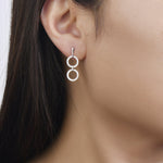 Load image into Gallery viewer, white gold dangling diamond earrings with two open circles connected by a metal bar on model. Unique jewelry, unique earrings. gladiator style earrings. on model