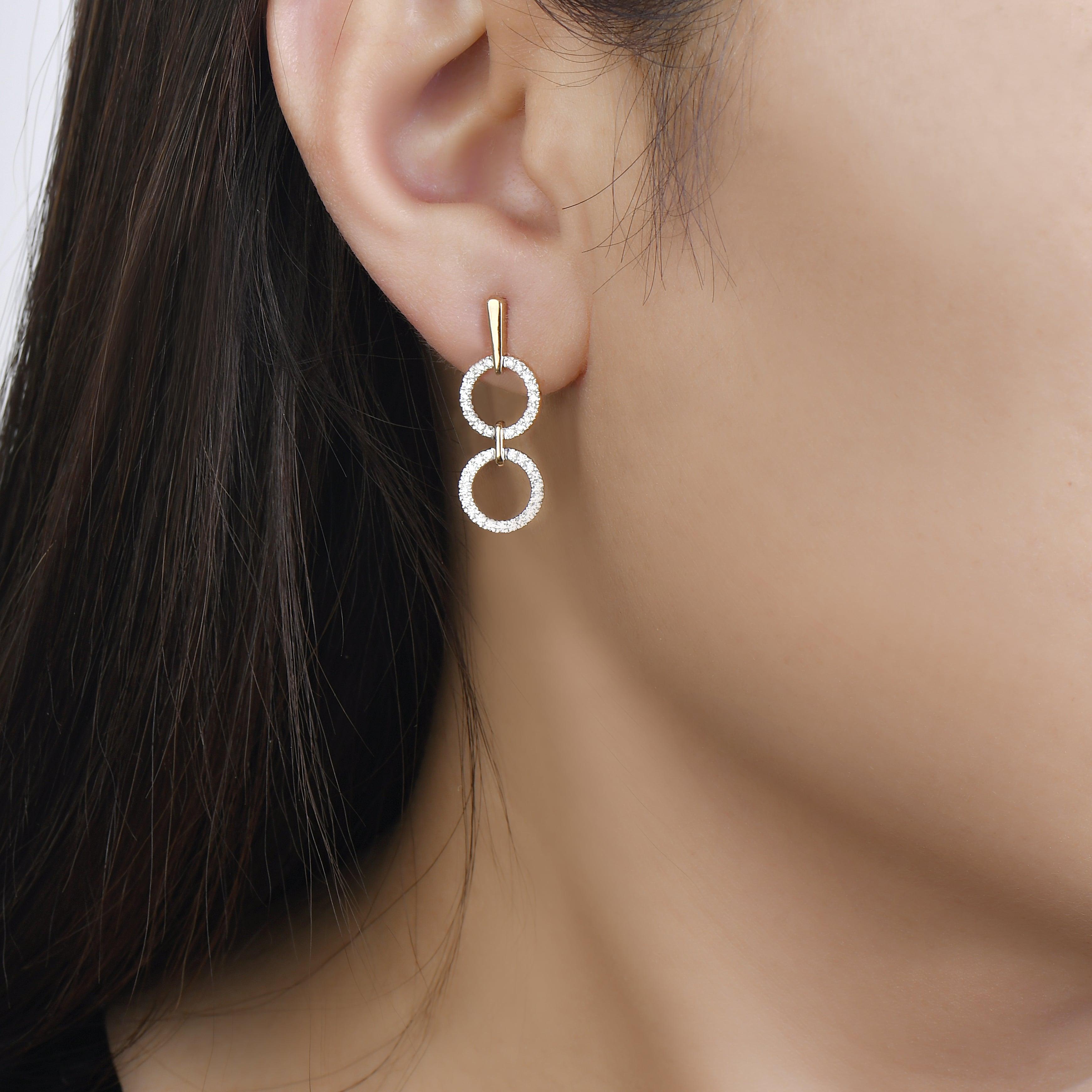unique jewelry, unique earrings, fashion jewelry, fashion earrings, diamond earrings in yellow gold, dangling earrings, dangling diamond earrings, drop earrings, diamond drop earrings, two circle shaped motifs hanging vertically connected in the middle by gold bar. Another gladiator like bar connects motifs to the post. on model