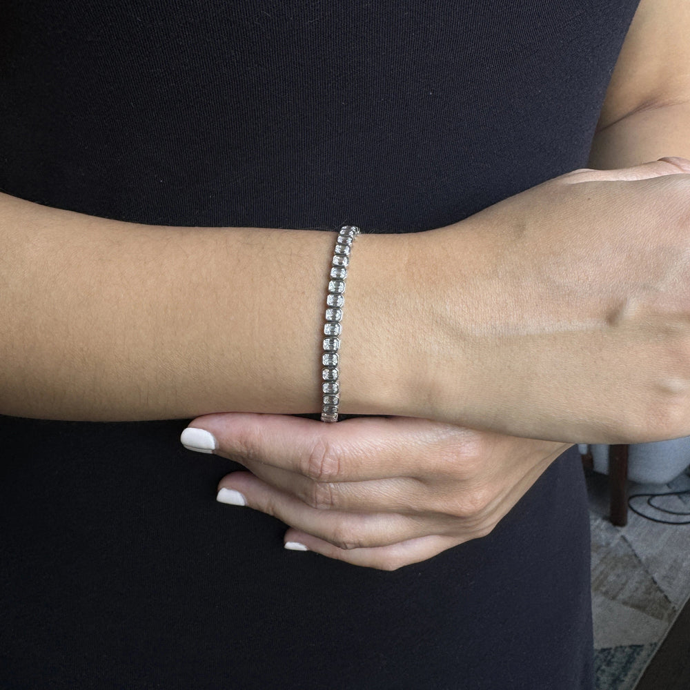 a white gold tennis bracelet with emerald cut diamonds in a bezel setting 