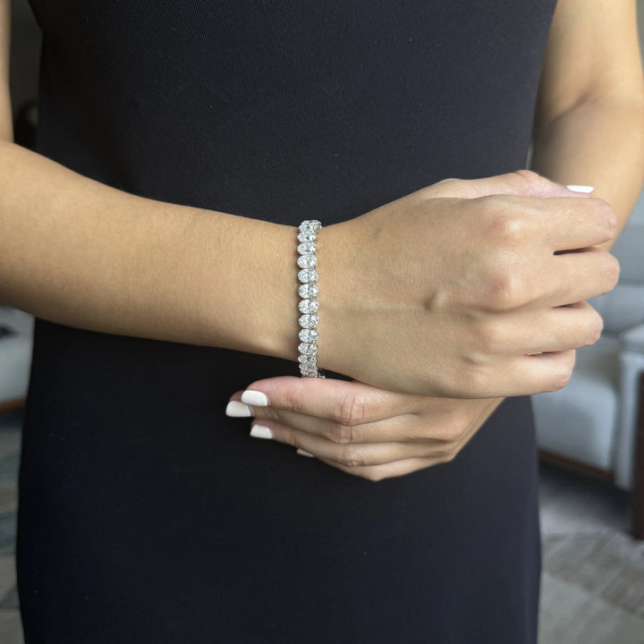 A close-up of a woman wearing an oval cut diamond tennis bracelet on her wrist.