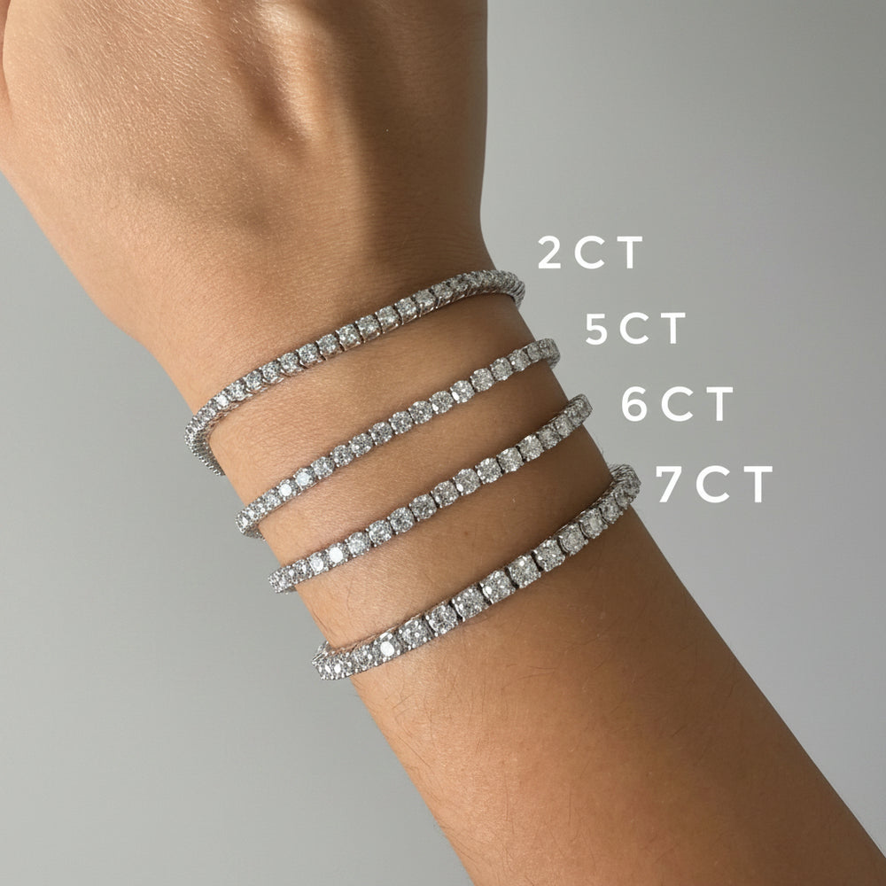 A close-up of a person's wrist wearing four white gold tennis bracelets with different stone counts: 2CT, 5CT, 6CT, and 7CT.