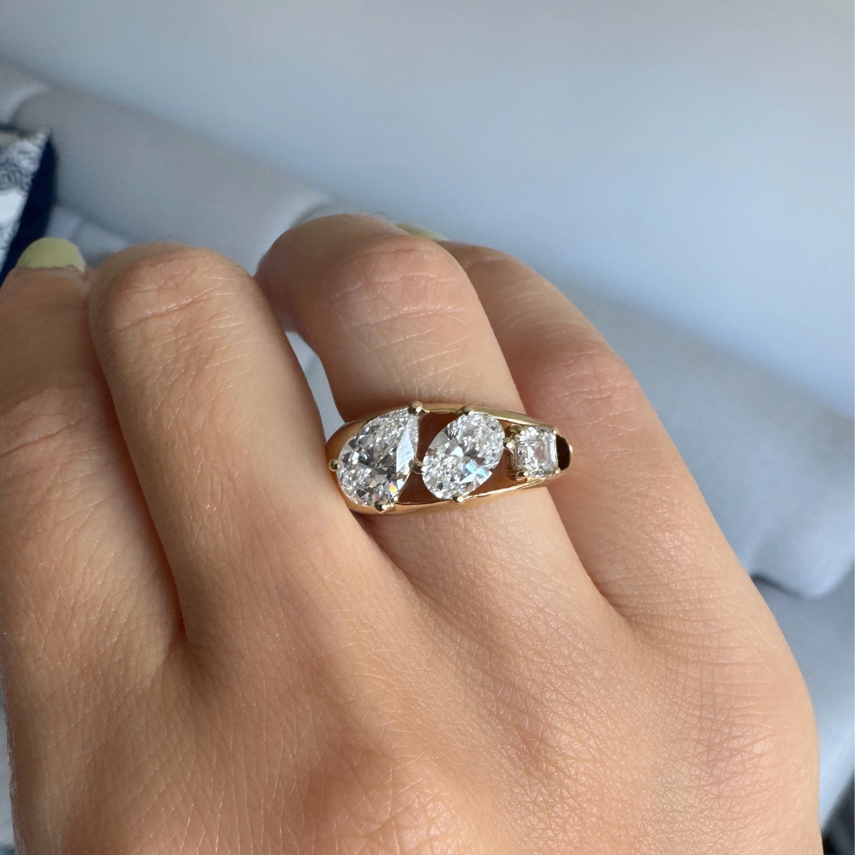 yellow gold three stone ring featuring a pear shaped diamond, an oval shaped diamond, and an asscher cut diamond worn on a hand