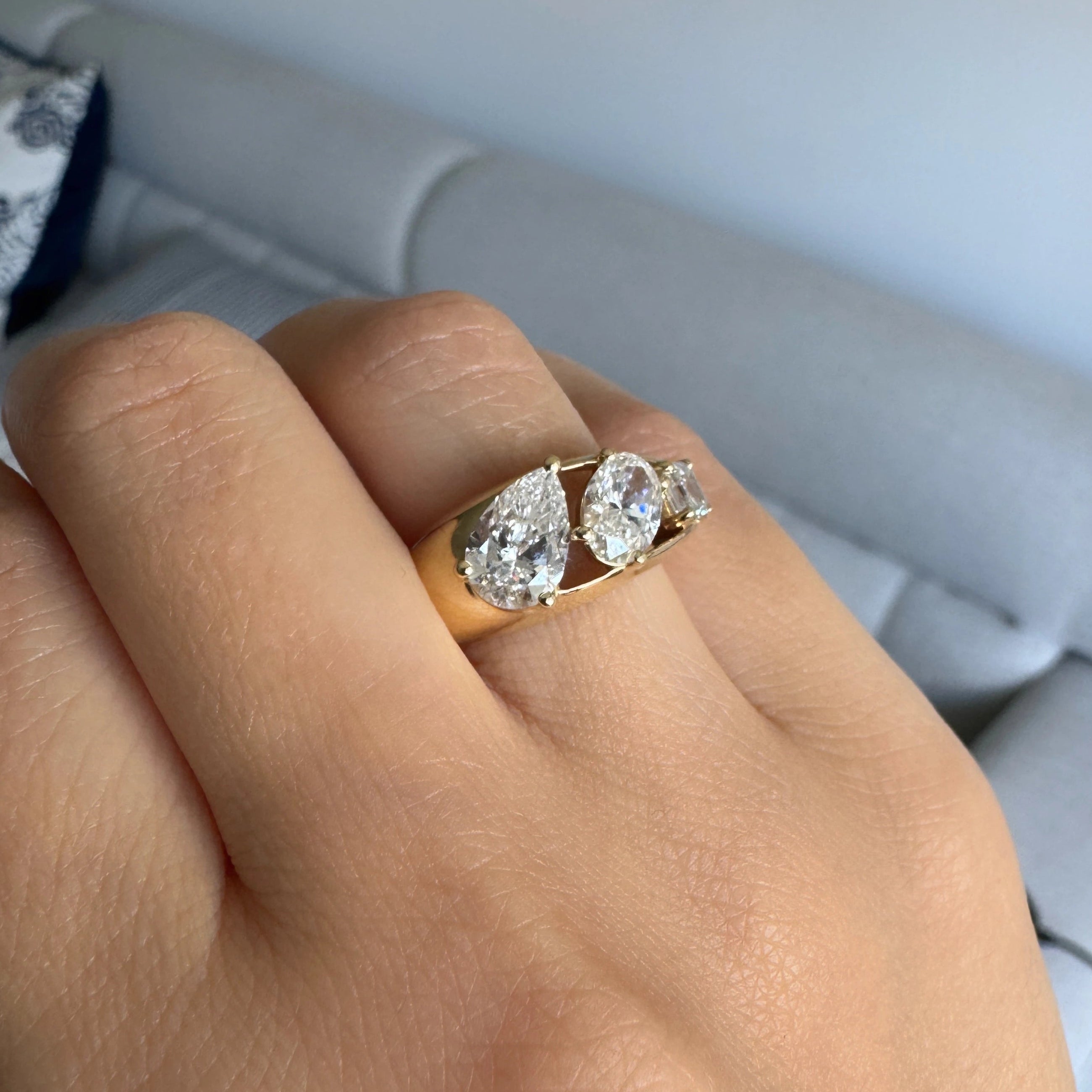 yellow gold three stone ring featuring a pear shaped diamond, an oval shaped diamond, and an asscher cut diamond worn on a hand showing a side view of the ring