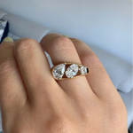yellow gold three stone ring featuring a pear shaped diamond, an oval shaped diamond, and an asscher cut diamond worn on a hand