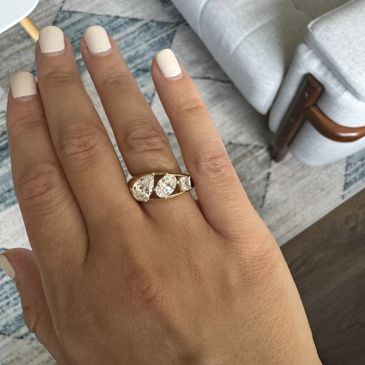 a three stone gold ring with a pear cut diamond, oval cut diamond, and Asscher cut diamond in descending size order.