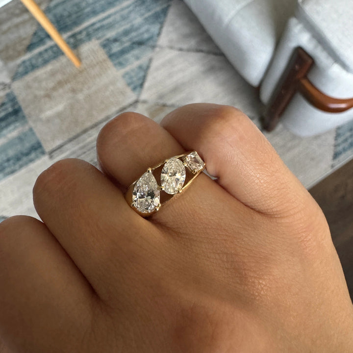 a three stone gold ring with a pear cut diamond, oval cut diamond, and Asscher cut diamond in descending size order.