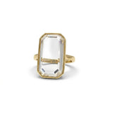 Portrait cut moissanite ring with a large emerald-shaped clear stone in a gold bezel setting.