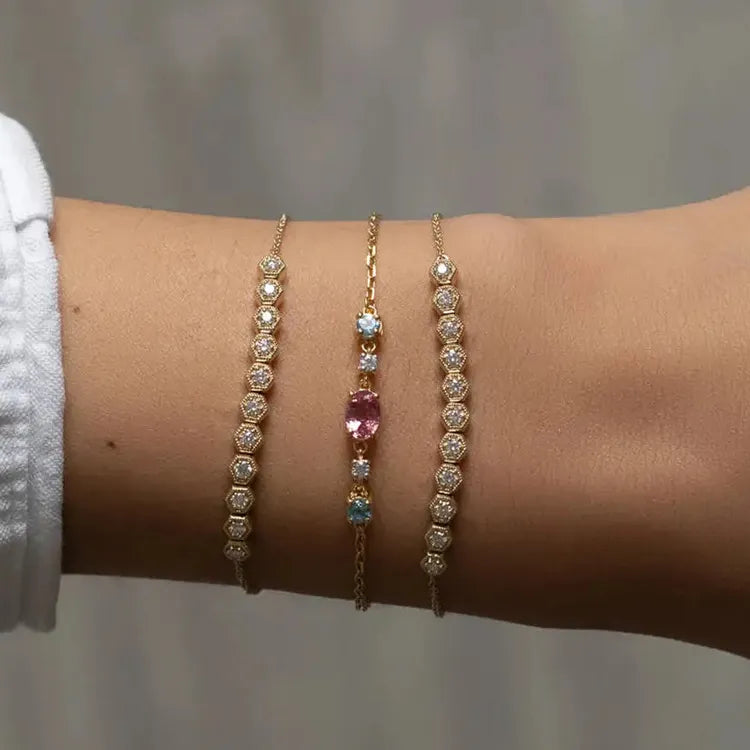 Model wearing stackable bracelets in yellow gold and 18k vermeil. Diamond bracelets and gemstone bracelets. gemstones are pink tourmaline, blue topaz, and white sapphire.