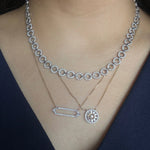 A close-up of a model wearing layering necklaces. The diamond necklaces include a white gold collar necklace with a repeating circular link pattern, a yellow gold diamond necklace with pave diamonds and baguette diamonds, and a matching yellow gold chain with a circular sunburst design also made of pave diamond and baguette diamonds.