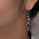 unique jewelry, unique earrings, fashion jewelry, fashion earrings, drop earrings in rose gold, dangling earrings, dangling drop earrings with a design of geometric shapes intertwined with each other. Earrings have a fishhook back. Earrings on model.